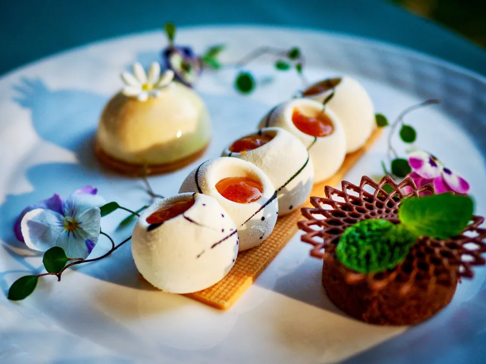 A plate of small cream domes with apricot centres, edible flowers and a chocolate lattice tart